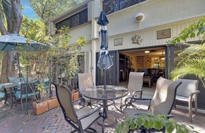 An outdoor patio area with a round glass table, four chairs, and a striped umbrella. - Exec Bay Resort-Style 4BR Townhome w/Beach, Marina, Heat/Chill Pool & Pickleball (Islamorada)