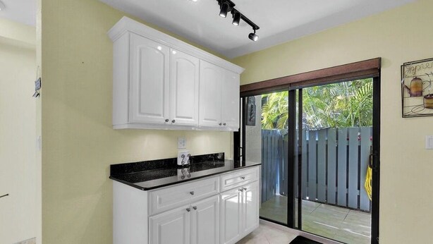 A kitchen with white cabinets, a black countertop, and a sliding glass door leading to a balcony. - Exec Bay Resort-Style 4BR Townhome w/Beach, Marina, Heat/Chill Pool & Pickleball (Islamorada)