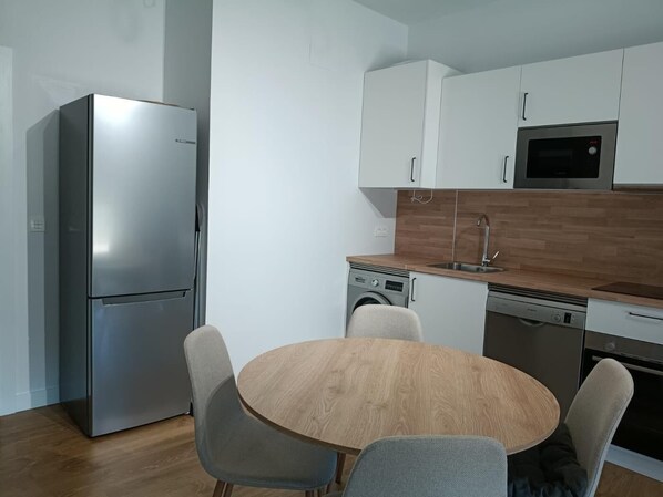 A modern kitchen with a stainless steel refrigerator, a microwave, a dishwasher, and a wooden dining table with chairs.