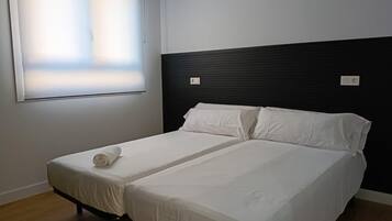 A double bed with white bedding in a room with a dark headboard and a window with blinds.