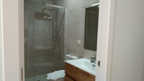 A modern bathroom with a glass-enclosed shower, a white sink, and a wooden vanity. - The Rooftop Apartment A (Basauri)