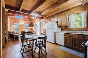 A wooden cabin interior with a dining area, kitchen, and a view of the forest. - Cliffline Sunset Views with New Hot Tub, Pet Friendly (Zoe)