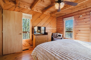 A wooden cabin bedroom with a bed, a dresser, a television, and a chair. - Cliffline Sunset Views with New Hot Tub, Pet Friendly (Zoe)