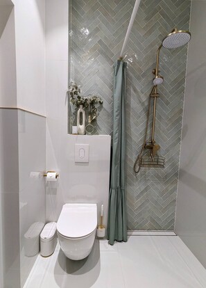 Une salle de bain moderne avec des toilettes blanches, une douche dotée d’un pommeau de douche doré et un mur orné d’un motif en chevrons.