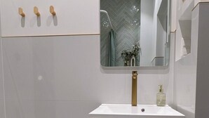 A modern bathroom with a white vanity, a large mirror, and a herringbone-patterned wall.