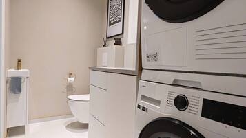 Une buanderie moderne avec des lave-linge et des sèche-linge superposés, des toilettes et une œuvre d’art encadrée accrochée au mur.