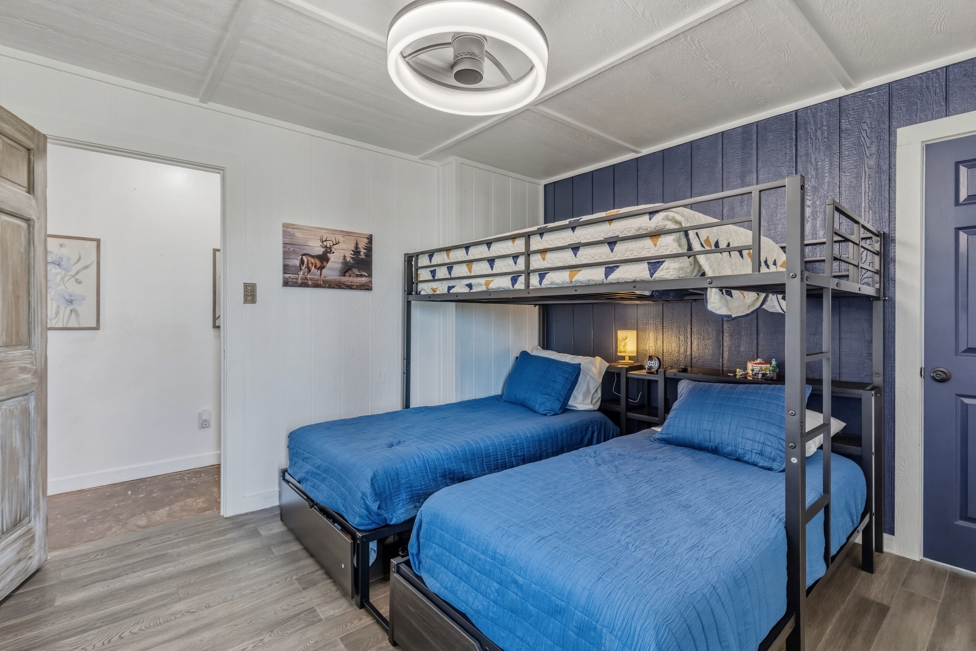 A room with two bunk beds, a ceiling light, a door, and a wall-mounted picture.