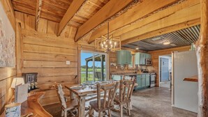 A rustic wooden interior with a dining area, kitchen, and large windows.
