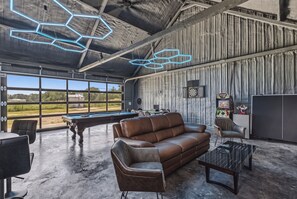 A spacious room with a pool table, leather sofa, and a dartboard.