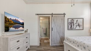 A bedroom with a wooden dresser, a bed with a floral bedspread, a sliding barn door, a framed picture of horses, and a large landscape painting on the wall.