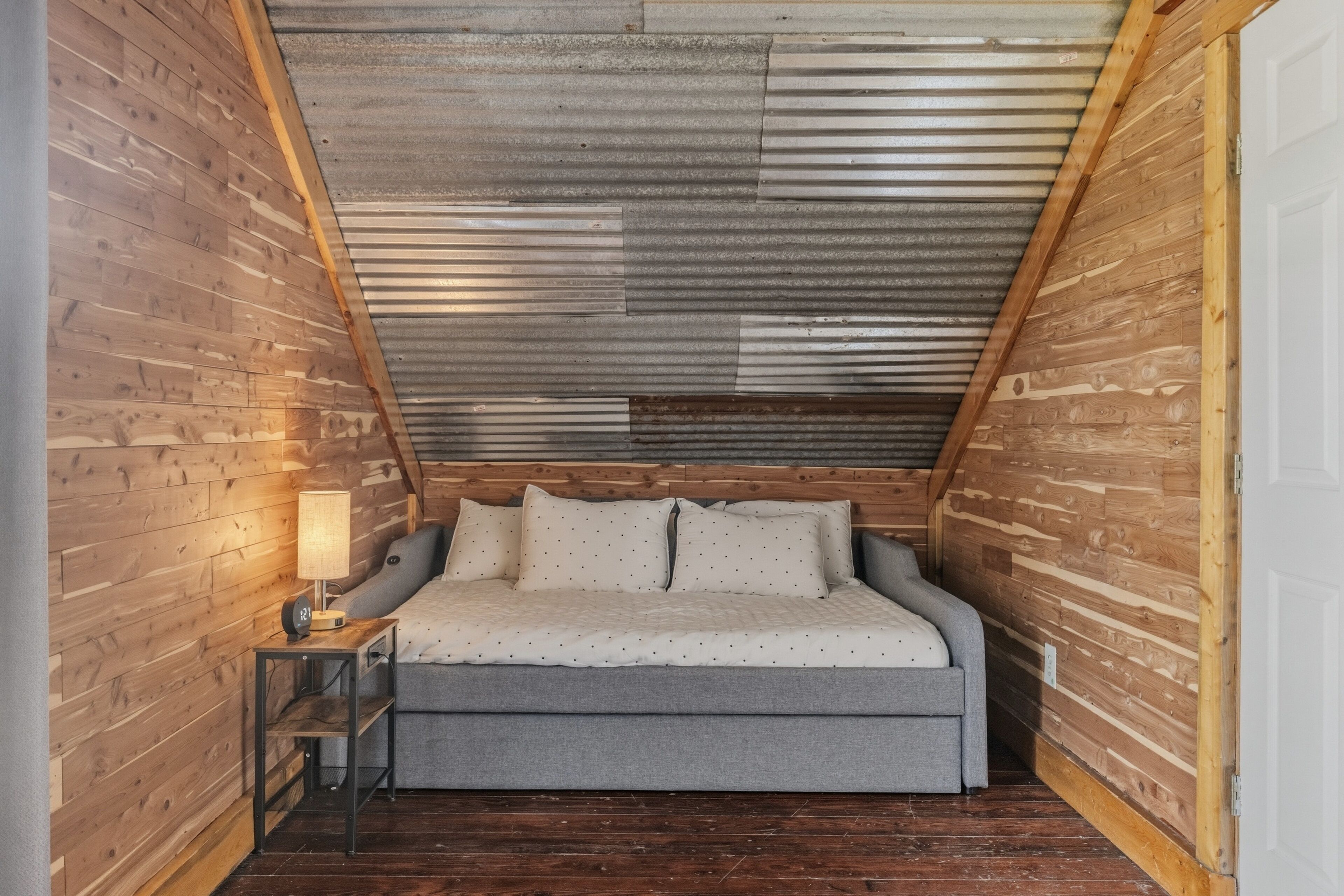Ein kleines, gemütliches Schlafzimmer im Dachgeschoss mit schrägen Wänden, einem Einzelbett, einem Nachttisch und einer Lampe.