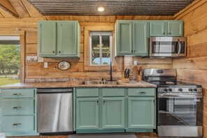 Una cocina con gabinetes verdes, lavavajillas de acero inoxidable, microondas y estufa.