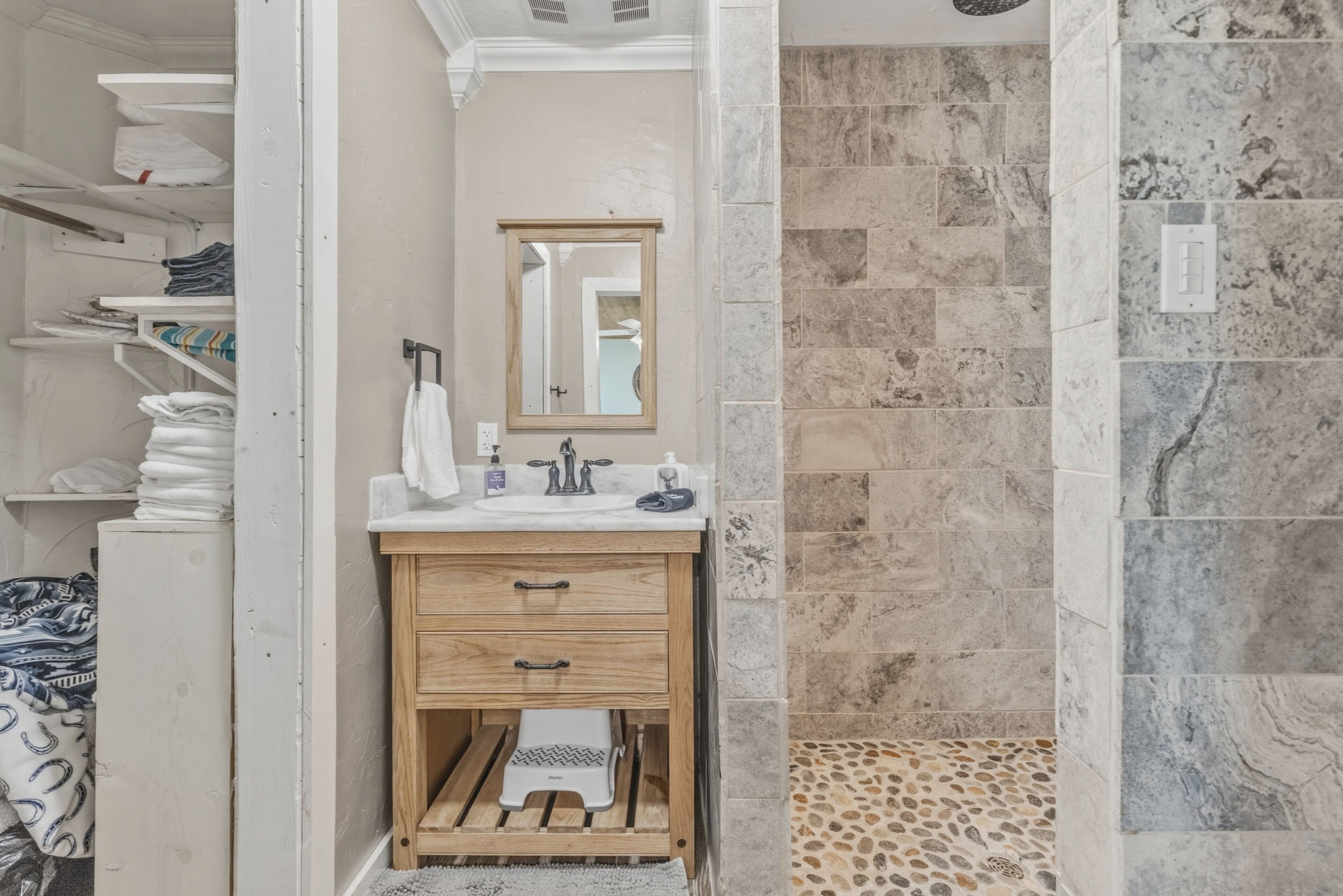 A bathroom with a wooden vanity, a mirror, a shower with a stone tile wall, and a towel rack.