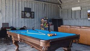 A billiards room with a pool table, chairs, and a couch.