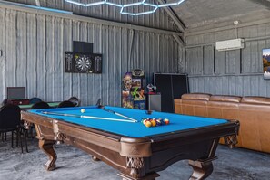 A billiards room with a pool table, chairs, and a couch.