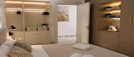 A modern bedroom with a large bed, a bedside table, a wardrobe, and a mirror.