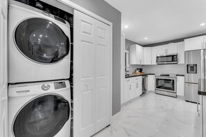 A modern kitchen with stainless steel appliances, a double washer, and a white tiled floor. - Azure Coastal Breeze • Near Lakes, Golf & Beaches (North Miami Beach)