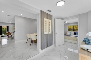 A modern interior with a dining area, a bed with a view, and a hallway leading to another room. - Azure Coastal Breeze • Near Lakes, Golf & Beaches (North Miami Beach)