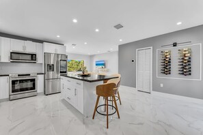 A modern kitchen with stainless steel appliances, a marble countertop, and a bar area with stools. - Azure Coastal Breeze • Near Lakes, Golf & Beaches (North Miami Beach)