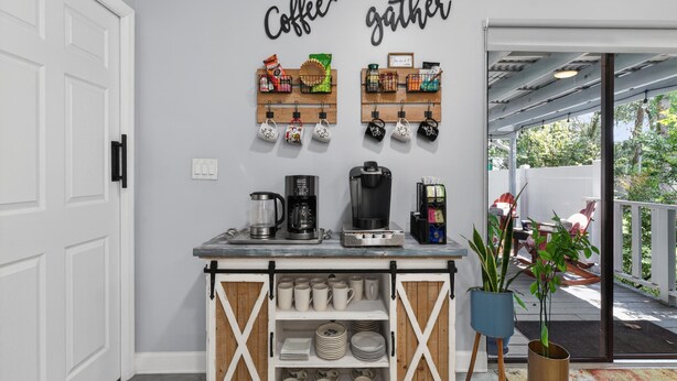 A kitchen area with a coffee station, a coffee maker, mugs, and a coffee grinder. - Backyard Oazis (St. Augustine)
