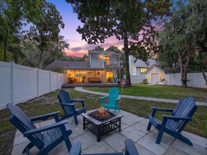 Ein Garten mit Feuerstelle, Sitzgelegenheit und einem Haus mit Terrasse.