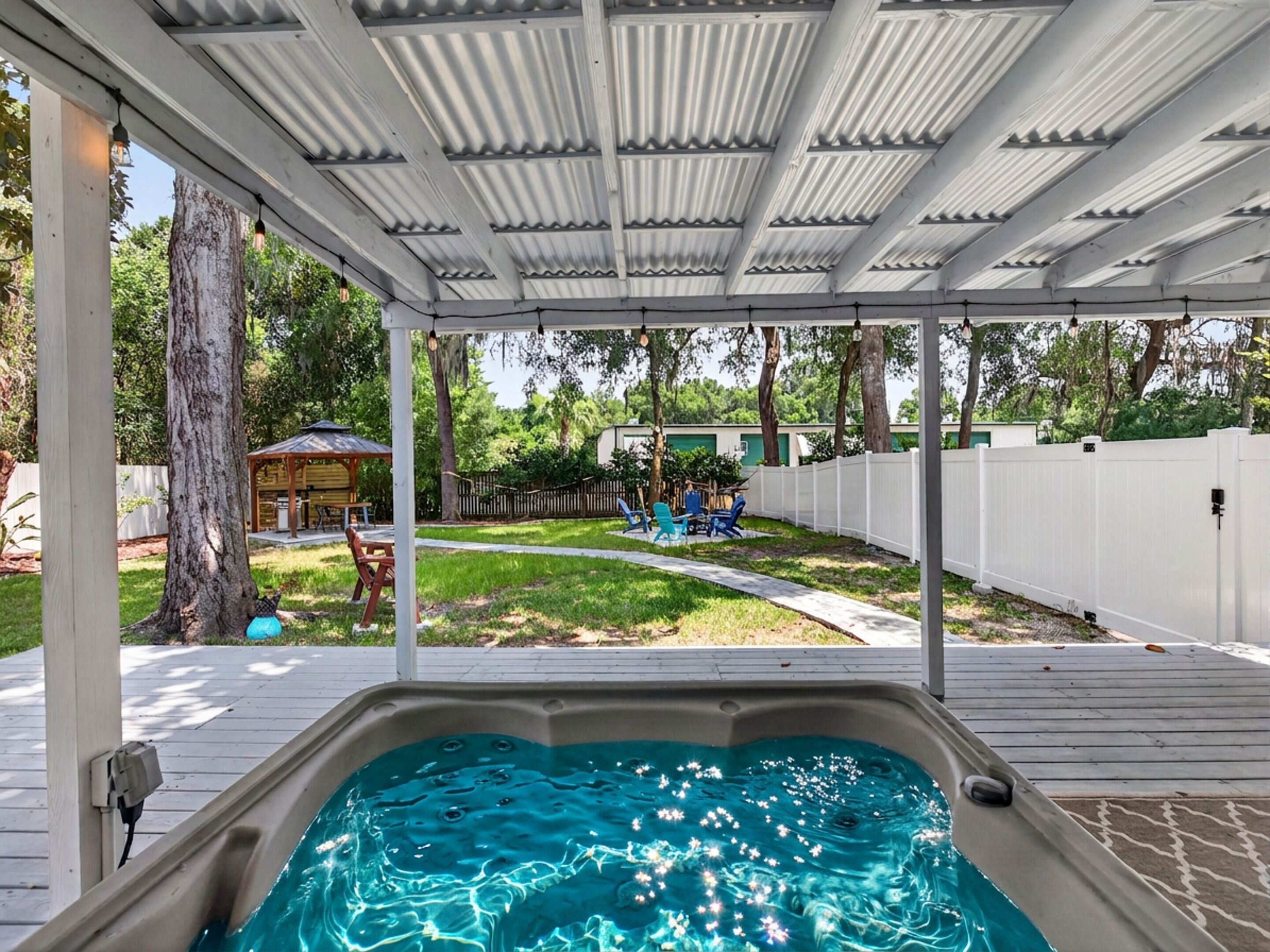Ett utomhusområde med en uppvärmd pool som är delvis skyddad, ett trädäck, en inhägnad trädgård och en pergola i bakgrunden.