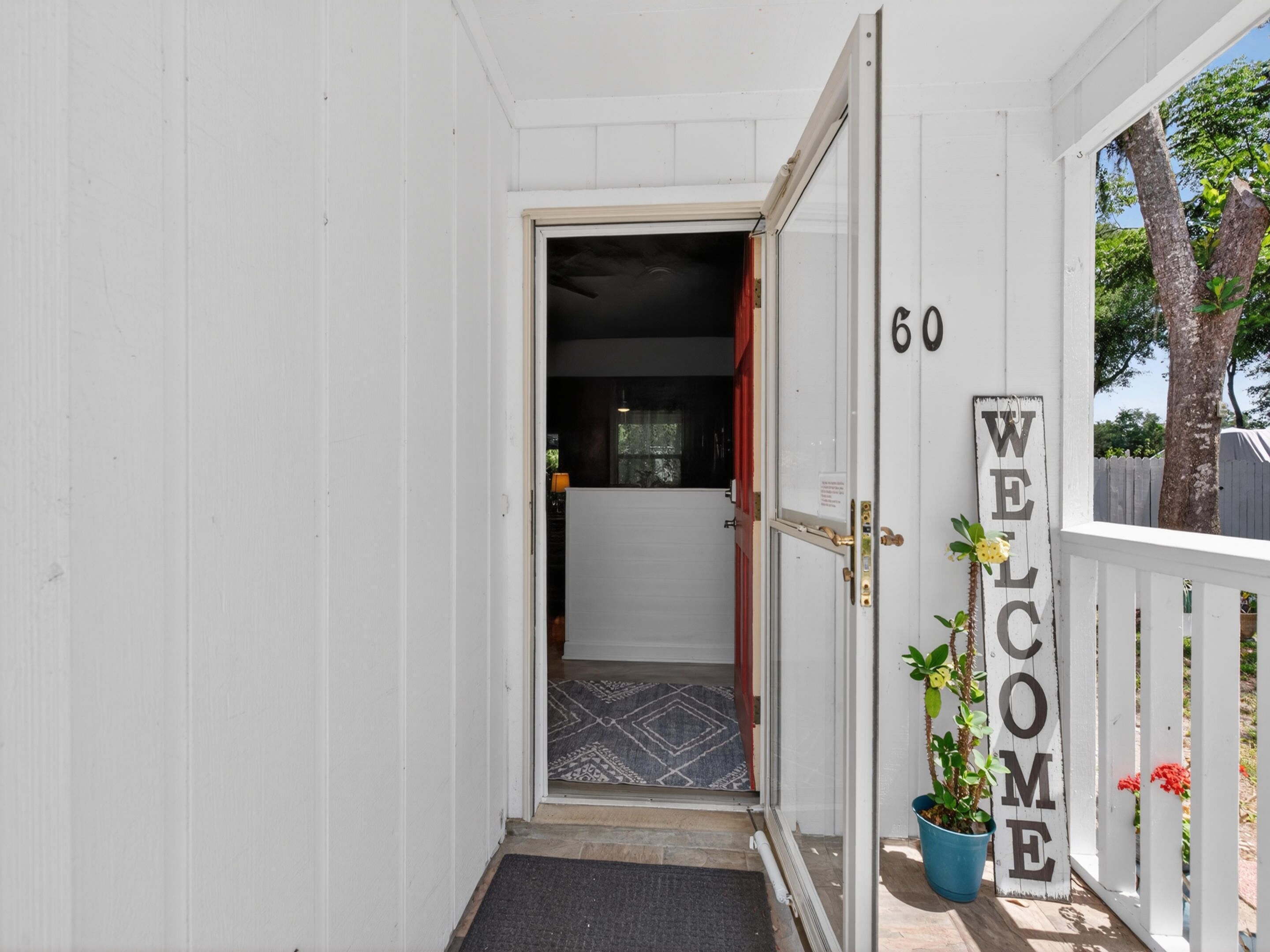 A white wooden door with a 'WELCOME' sign, a number '60' on the wall, and a potted plant.