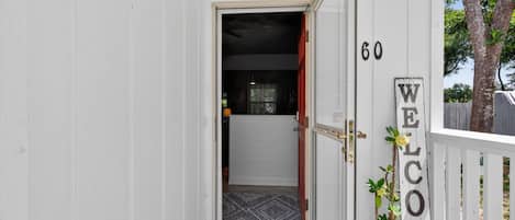 A white wooden door with a 'WELCOME' sign, a number '60' on the wall, and a potted plant.