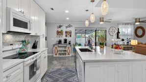 A modern kitchen with white cabinetry, a central island, and pendant lighting. - Backyard Oazis (St. Augustine)