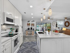 A modern kitchen with white cabinetry, a central island, and pendant lighting. - Backyard Oazis (St. Augustine)