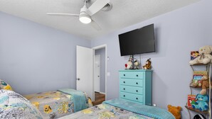 A bedroom with two beds, a ceiling fan, a TV, and a dresser with stuffed animals. - Backyard Oazis (St. Augustine)