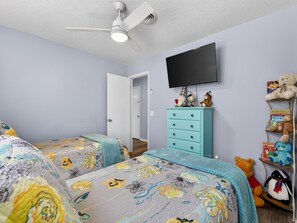 A bedroom with two beds, a ceiling fan, a TV, and a dresser with stuffed animals. - Backyard Oazis (St. Augustine)