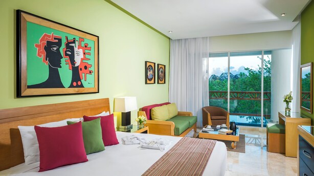 Une chambre d’hôtel avec un grand lit, un canapé, un bureau et une vue sur la verdure.