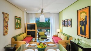 A modern living room with a dining area, featuring a glass-top table, colorful sofas, and artwork on the walls.