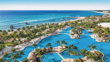 Een resort met meerdere zwembaden, palmbomen en een strand.