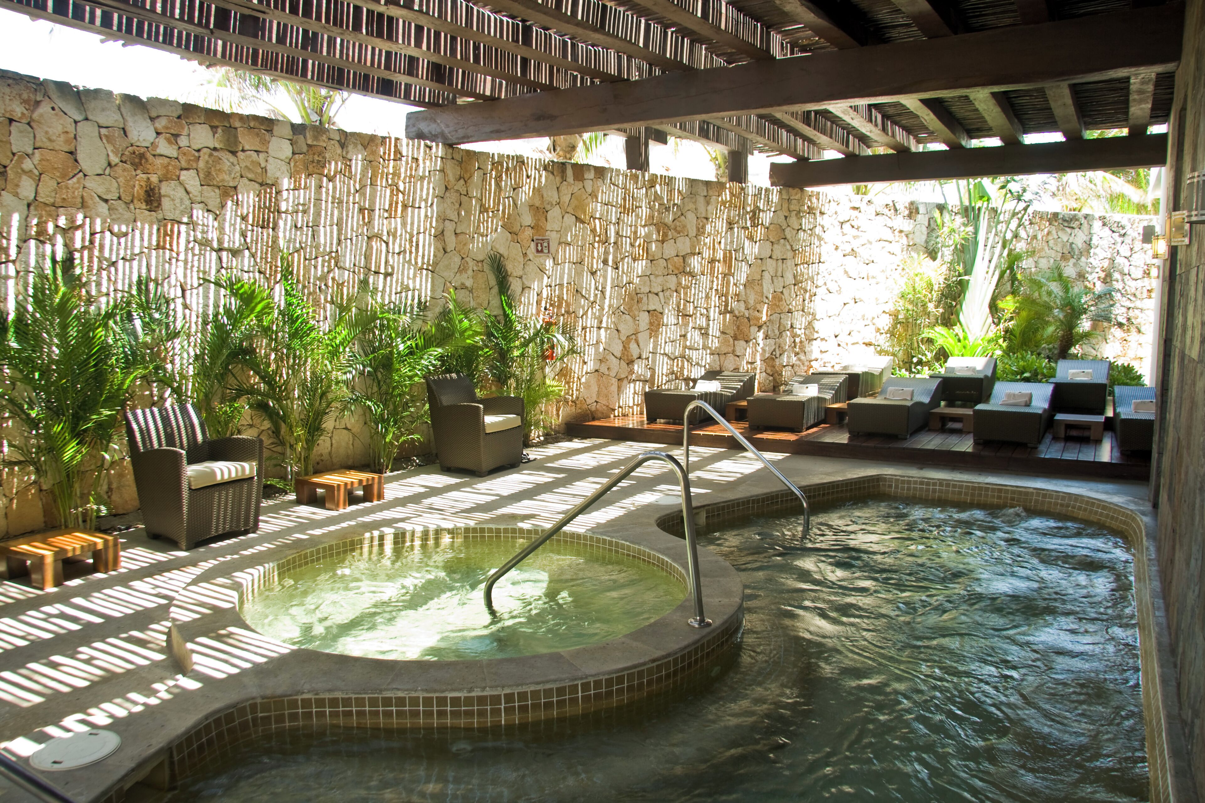 A spa area with a hot tub, lounge chairs, and a stone wall.