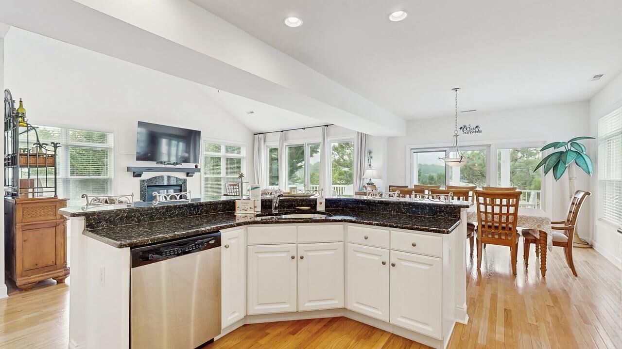 A modern kitchen with a large island, white cabinetry, and a dining area with wooden chairs.
