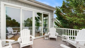 Eine überdachte Terrasse mit weißen Adirondack-Stühlen und einer Glastür, die zu einem Innenraum führt.
