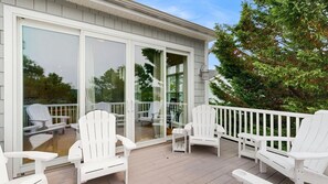 Eine überdachte Terrasse mit weißen Adirondack-Stühlen und einer Glastür, die zu einem Innenraum führt.