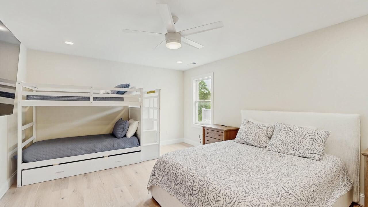 Un dormitorio con una cama individual, una litera, una mesita de noche y un ventilador de techo.