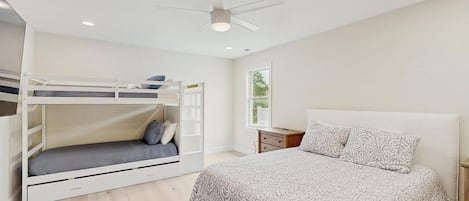 Un dormitorio con una cama individual, una litera, una mesita de noche y un ventilador de techo.