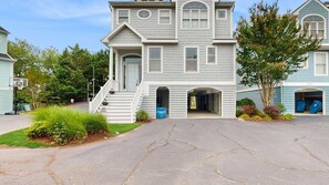 A two-story residential building with a front entrance, a visible garage door, and a driveway leading to the entrance. - Spacious home with large kitchen, outdoor shower, kayak launch access (Bethany Beach)