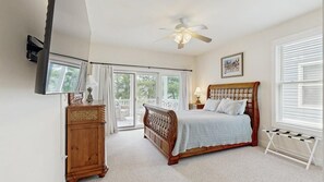 Een slaapkamer met een bed, een houten dressoir, een plafondventilator, een raam met jaloezieën en een foto aan de muur.
