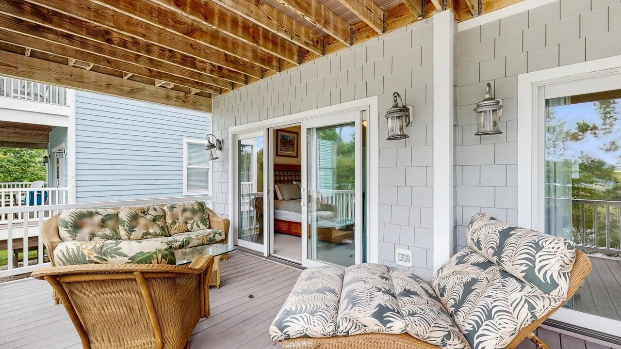 A covered porch with wicker furniture, glass doors leading to a bedroom, and wall-mounted lanterns.