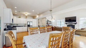 Eine geräumige Küche mit weißen Schränken, ein Essbereich mit Tisch und Stühlen, ein Wohnzimmer mit einer Couch und ein Kamin.