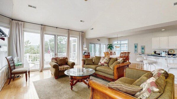 Een ruime woonkamer met een groot raam, een eethoek met een keuken op de achtergrond en een balkon met een Amerikaanse vlag.