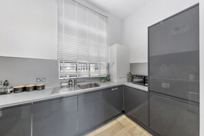 A modern kitchen with grey cabinets, a stainless steel sink, and a built-in microwave. - The City Retreat (London)