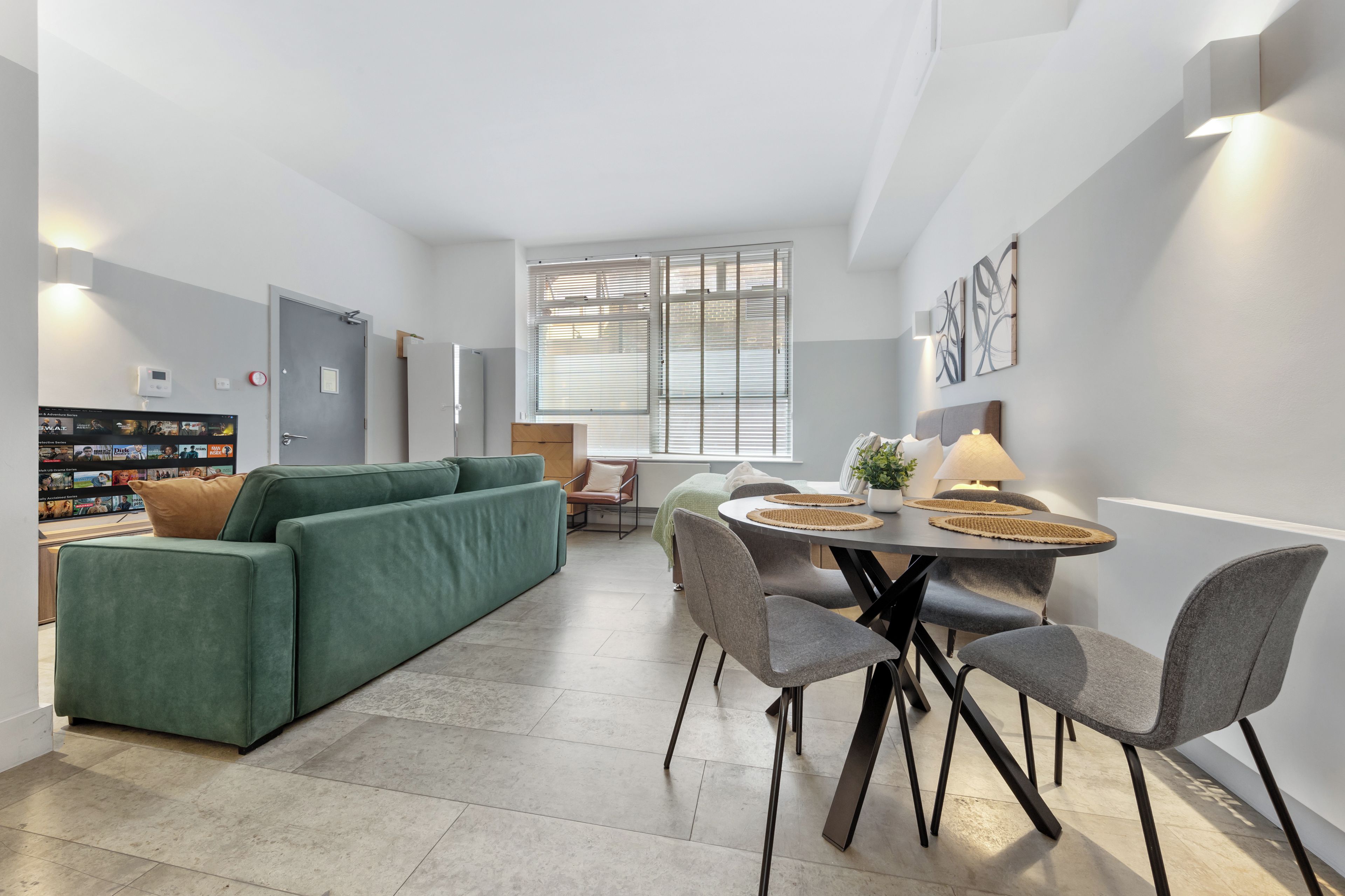 Un salon moderne avec un canapé vert, une table à manger avec des chaises et un téléviseur fixé au mur.