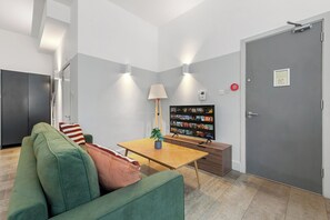A modern living room with a green sofa, a wooden coffee table, and a flat-screen TV displaying a movie selection. - The City Retreat (London)