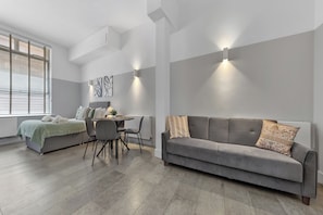 A modern living room with a grey sofa, a dining table with chairs, and a large window with blinds. - The City Retreat (London)